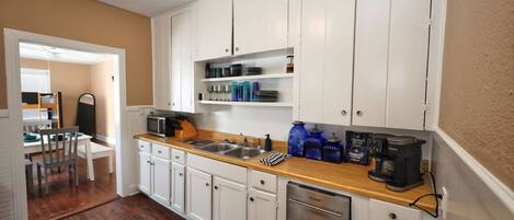 A compact kitchen with white cabinets, a wooden countertop, and a built-in dishwasher.
