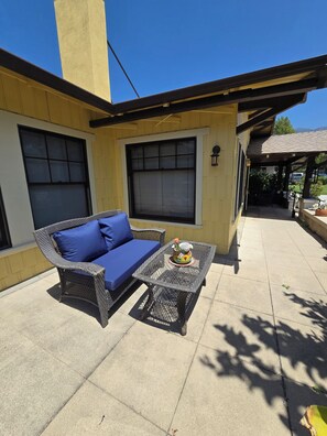 A patio area with a wicker sofa and a table, a covered seating area, and a building with large windows. - Historic 3BR Monrovia Oasis with Pool, BBQ & Spa (Monrovia)