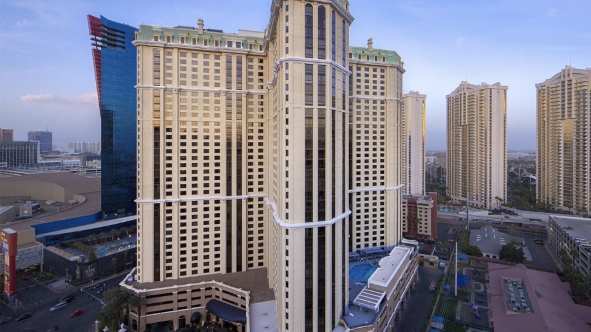 A high-rise building with multiple floors, a prominent corner structure, and a parking area in the foreground.