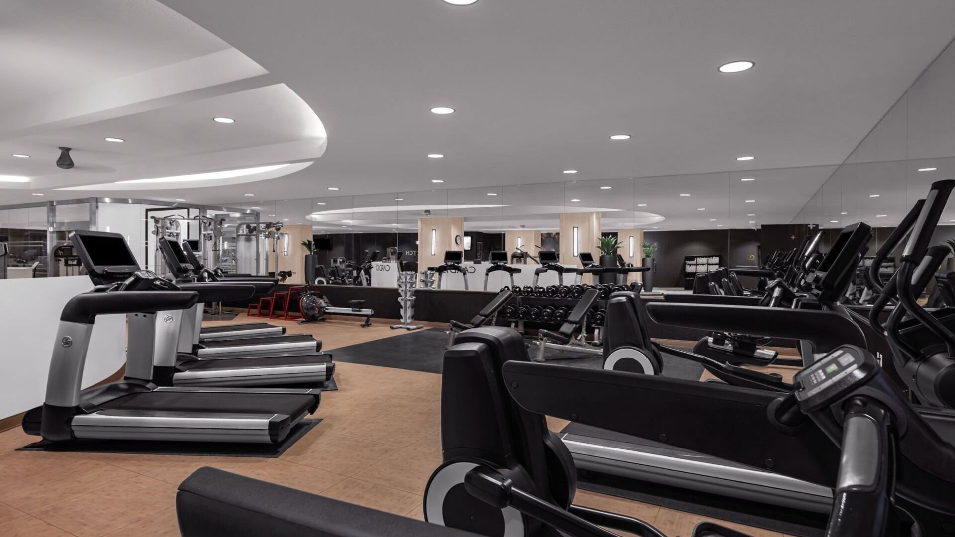 A modern gym with multiple treadmills, weight machines, and a cardio area.