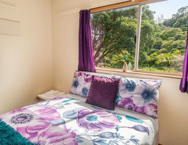 A bedroom with a bed, a window, and a view of greenery outside.