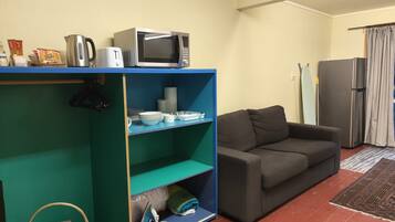 A living room with a blue shelving unit, a grey sofa, a refrigerator, and a striped curtain.