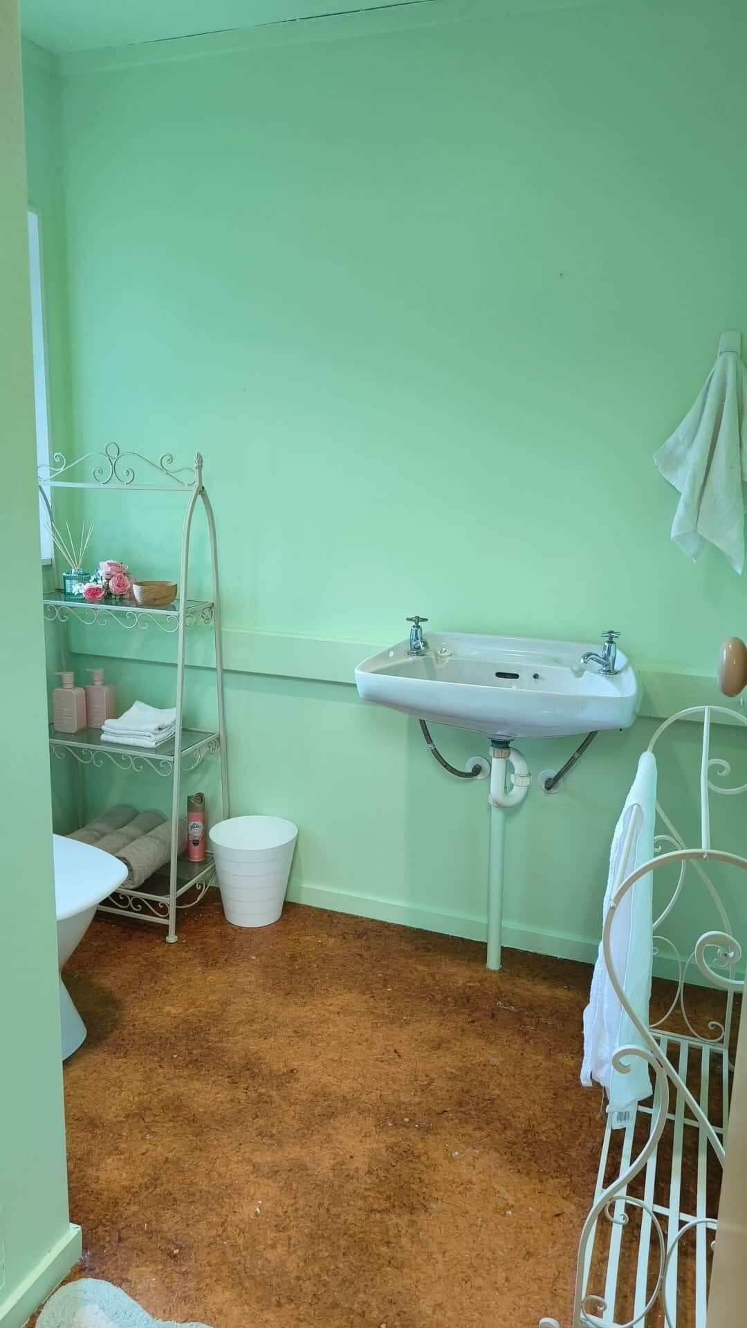 A bathroom with a white sink, a metal shelf with toiletries, a white bucket, and a white bathtub.