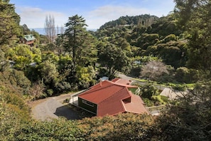 A house with a red roof, surrounded by dense greenery and hills in the background.