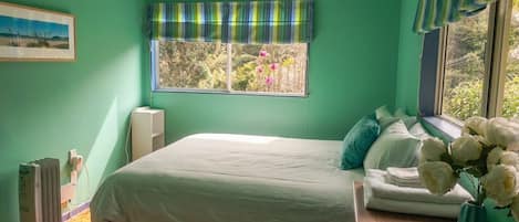 A room with a bed, a window with a view of trees, a radiator, and a framed picture on the wall.