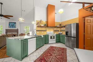 A kitchen with green cabinets, a white island, a stainless steel refrigerator, and a red patterned rug.