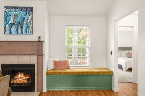 A room with a fireplace, a window with blinds, a green bench, and a painting on the wall.