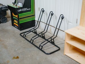 A metal rack with four hooks against a white wall, a wooden shelf unit to the right, and a black machine with green accents labeled 'MIDWAY CLASSIC ARCADE' in the background.