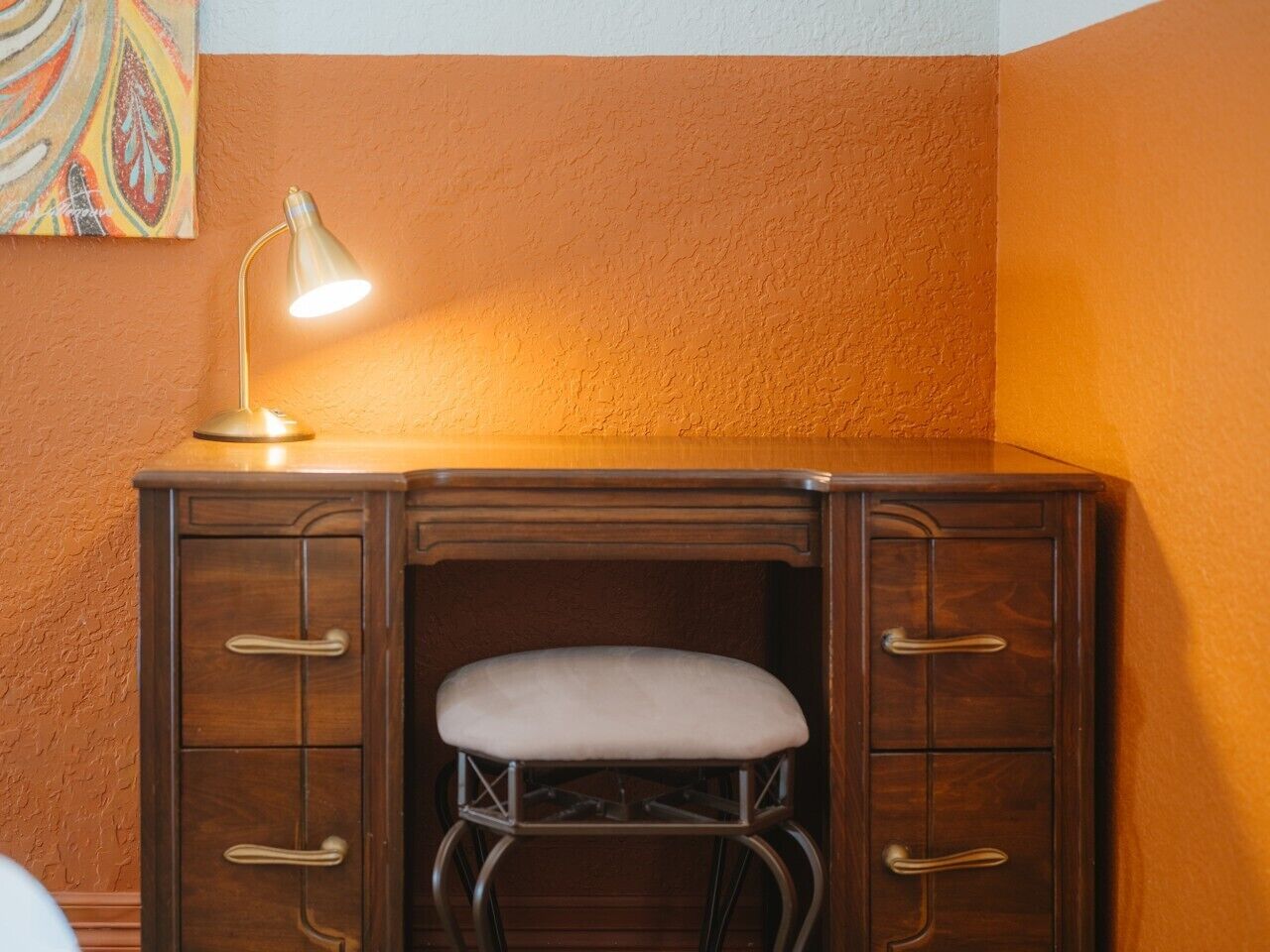 Un escritorio de madera con un asiento acolchado y una lámpara de escritorio.