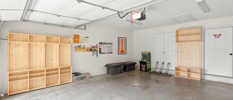 Un garage avec un sol en béton, des étagères en bois, un établi, une porte et un ventilateur de plafond.