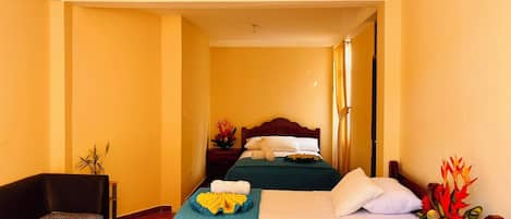 A hotel room with two beds, a sofa, a small table, and a potted plant.