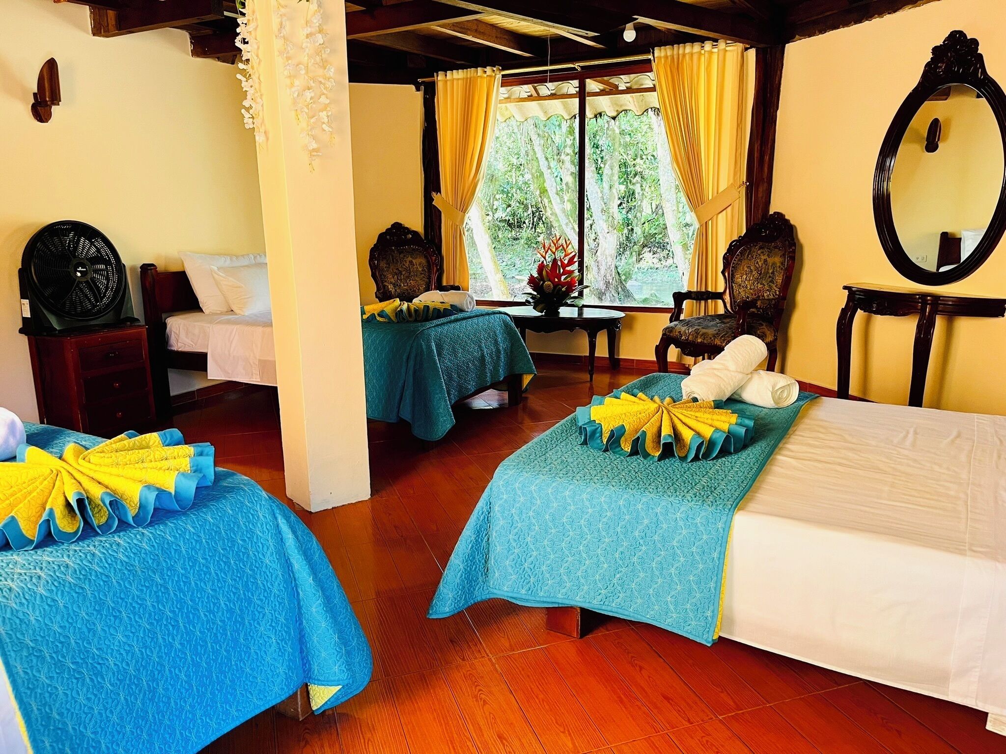 A hotel room with two beds, a sitting area, and a view of greenery through the window.