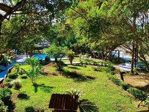 A pool area with a grassy lawn, trees, and a thatched-roof structure. - Hosteria Chuquitos Chalupas (Tena)