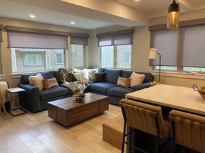 A modern living room with a sectional sofa, a coffee table, and a dining area with a table and chairs. - Luxury 3BR/3BA Basecamp Steps to Quicksilver Lift Main Street Dining Heated Pool (Breckenridge)