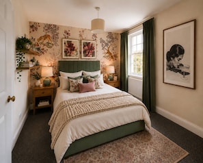 Un dormitorio con cama, mesitas de noche, lámpara, ventana con cortinas y un papel tapiz floral en la pared.