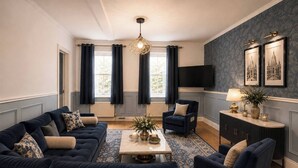 A living room with a dark blue sofa set, a coffee table, a side table with a lamp, and a television mounted on the wall.