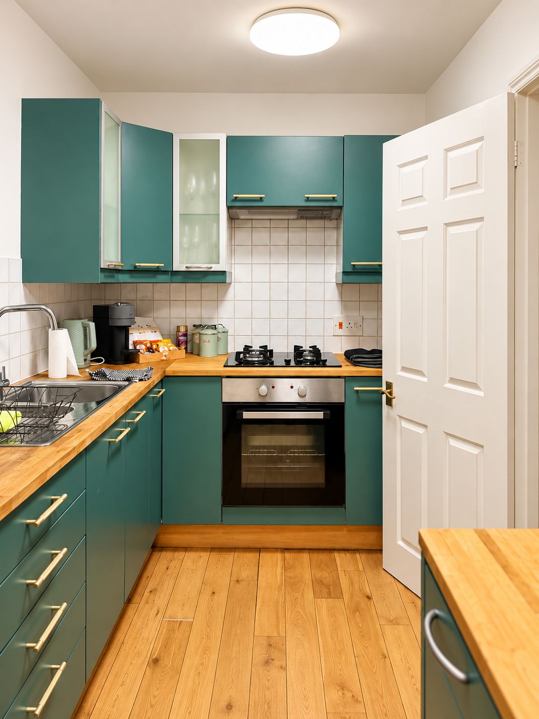Une cuisine compacte avec des meubles de couleur turquoise, un plan de travail en bois, une cuisinière à gaz et un four encastré.