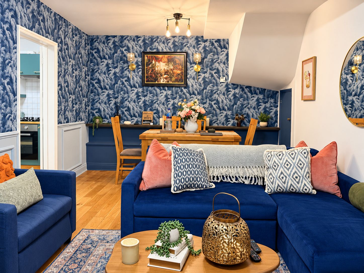 Ein Wohnzimmer mit einem blauen Sofa, einem Holzesstisch und einer durchgehenden Tür sichtbaren Küche.