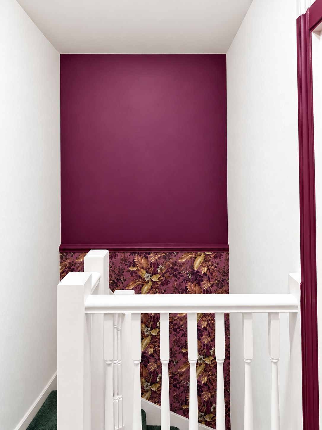 Eine Treppe mit weißen Balustern und einer weißen Handlauf, die zu einer Empore mit einer violetten Wand und floralem Wandpapier führt.