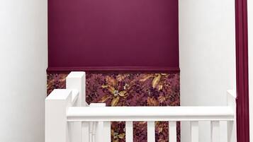 Eine Treppe mit weißen Balustern und einer weißen Handlauf, die zu einer Empore mit einer violetten Wand und floralem Wandpapier führt.