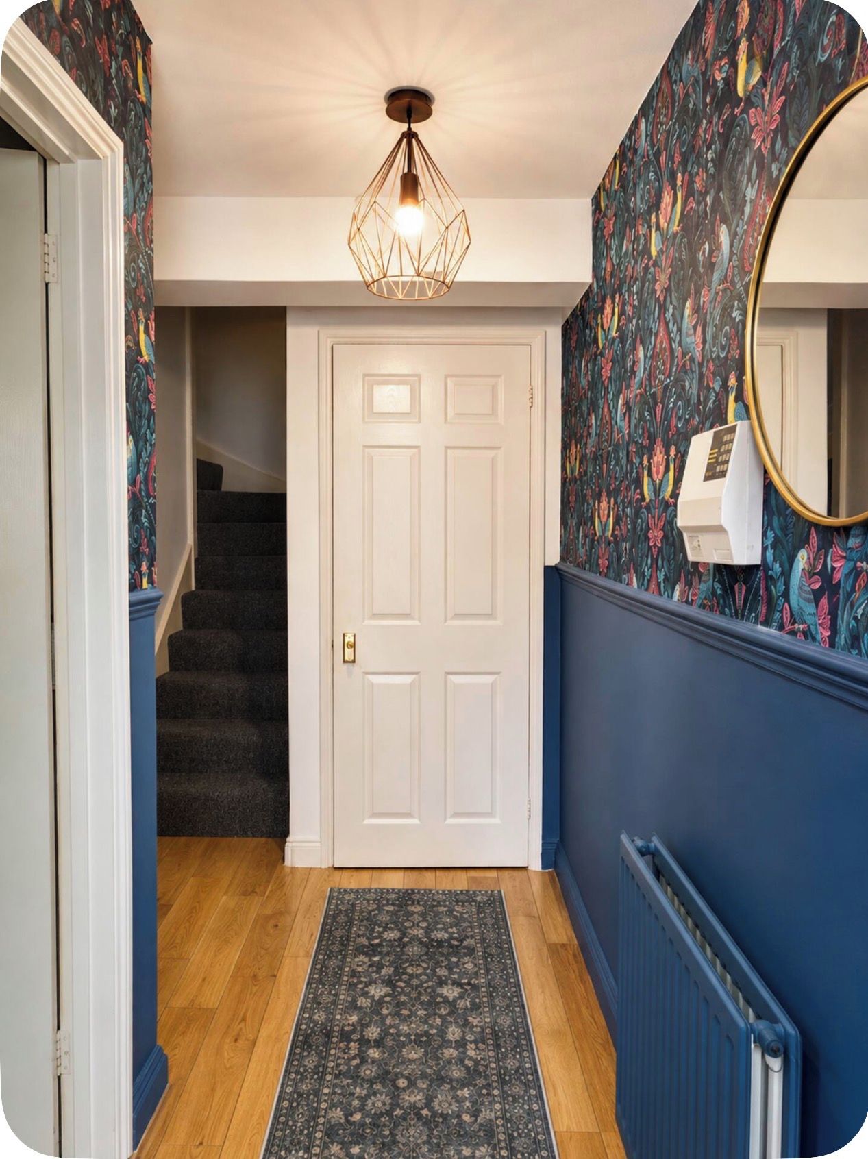 A hallway with a carpeted floor, a white door, a staircase, and a wall with a floral pattern.