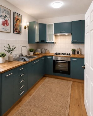 A modern kitchen with teal cabinets, a stainless steel sink, and a gas stove.