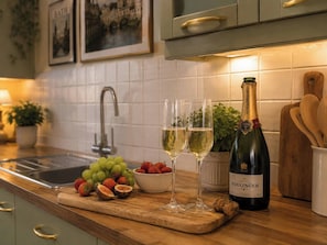 A kitchen counter with a bottle of Bollinger champagne, two glasses, a bowl of strawberries, and a pile of grapes.