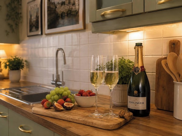 Una encimera de cocina con una botella de Bollinger champagne, dos copas, un bol de fresas y un montón de uvas.