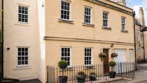 A two-story building with multiple windows, a door, and a small garden area with potted plants.