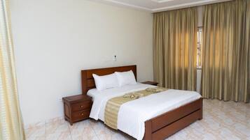 Quarto de hotel com cama de madeira, mesa de cabeceira e janela com cortinas.
