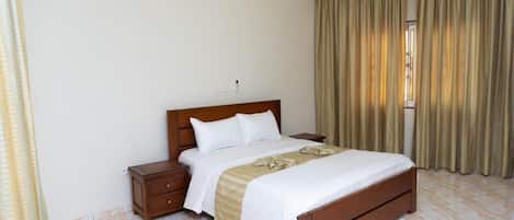 A hotel room with a wooden bed, a nightstand, a bedside table, and a window with curtains.