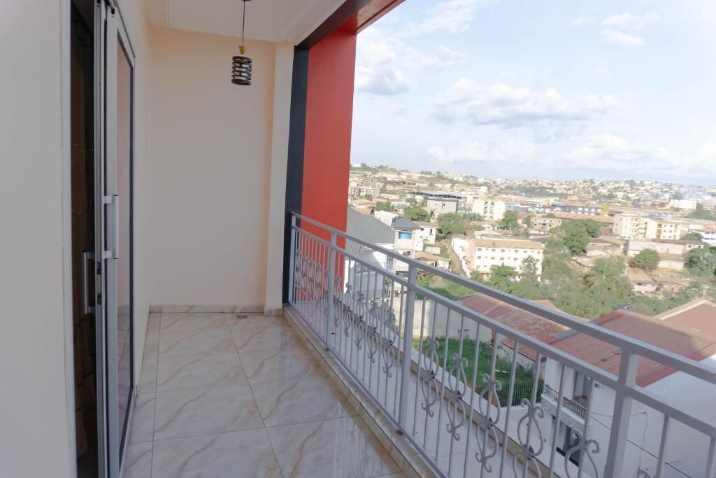 Uma varanda com guarda-corpo de metal, um pilar vermelho e vista para um horizonte urbano.