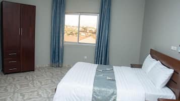 Un dormitorio con cama, armario, ventana con cortinas y vista al exterior.