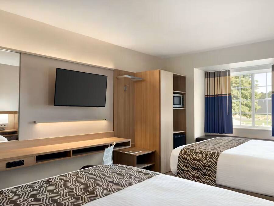 Una habitación de hotel con una cama, televisión en la pared, escritorio y armario.