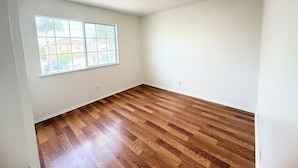 Ein Zimmer mit Holzboden, einem großen Fenster und weißen Wänden.