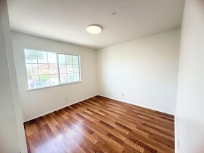 Una habitación con piso de madera, un ventanal grande y paredes blancas.