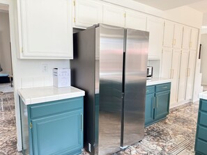 A kitchen with teal cabinets, a stainless steel refrigerator, and a white countertop.