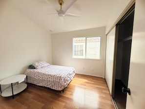 A bedroom with a bed, a small table, a ceiling fan, and a window with a view.