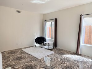 A room with patterned floor tiles, a black chair, a small white table, and a window with curtains.