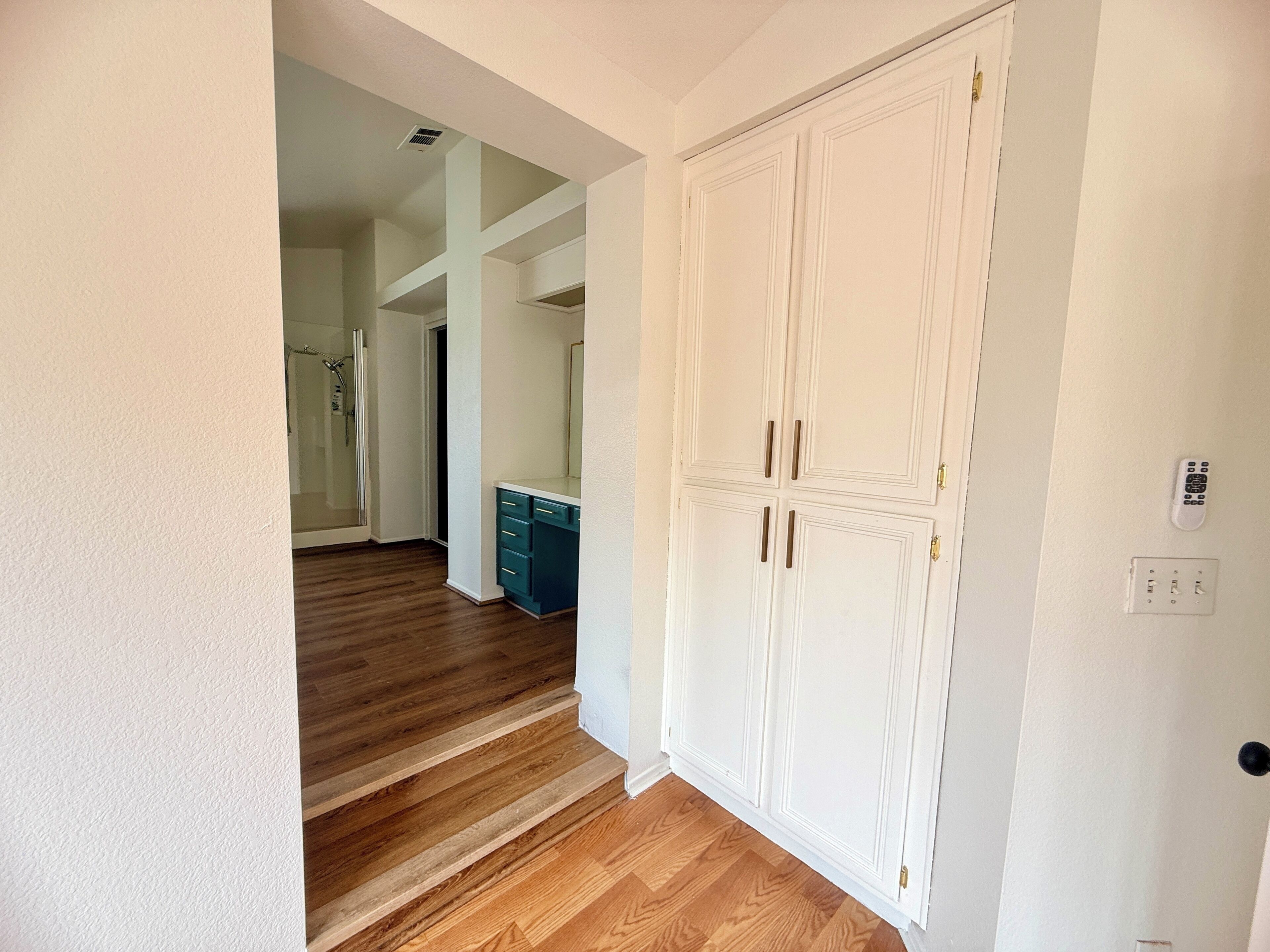 Ein Flur mit Holzboden, einer weißen Tür mit zwei Griffen und einem Lichtschalter an der Wand.