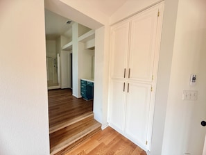 A hallway with wooden flooring, a white door with two handles, and a light switch on the wall.