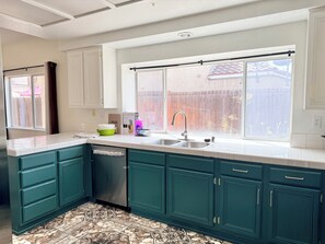 Una cocina con armarios color turquesa, un lavamanos de acero inoxidable y una ventana con vistas a una valla de madera.