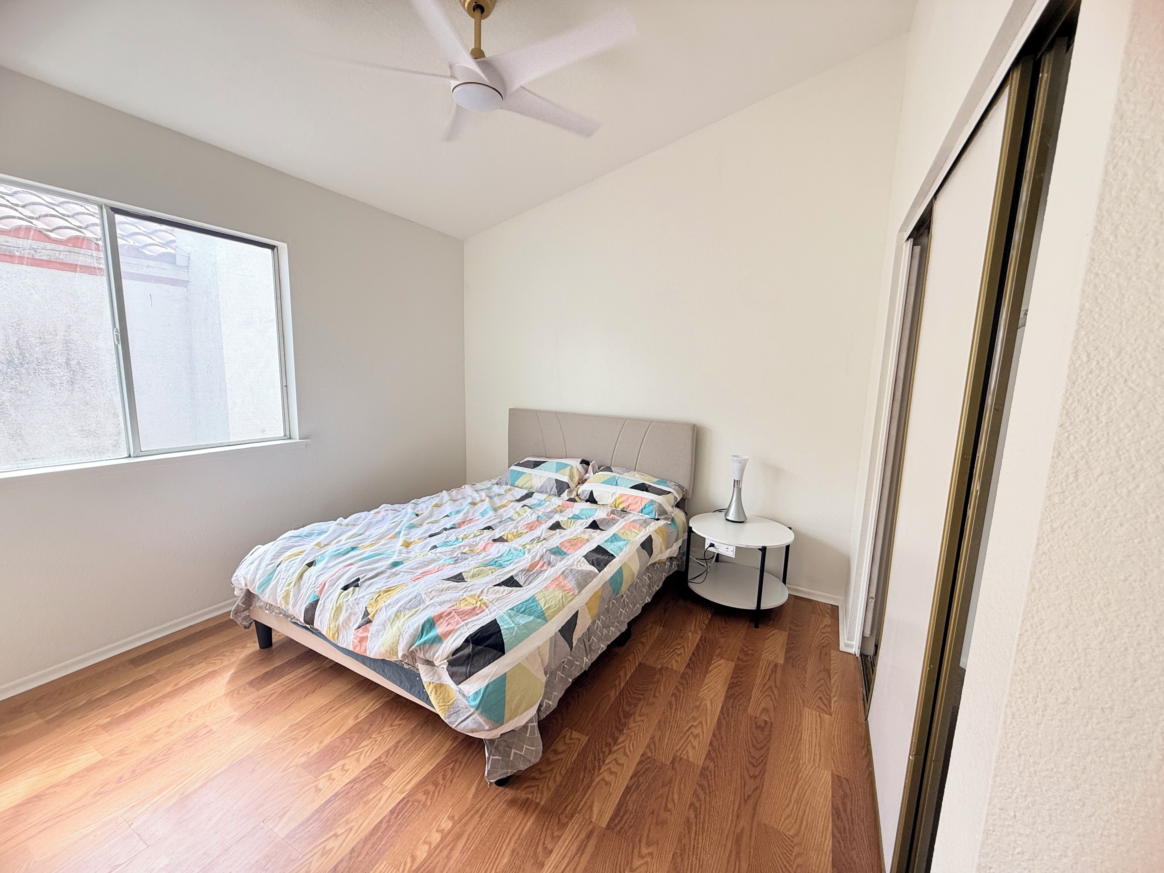 Ein Schlafzimmer mit einem Bett, einem Nachttisch, einem Deckenventilator und einem Fenster.