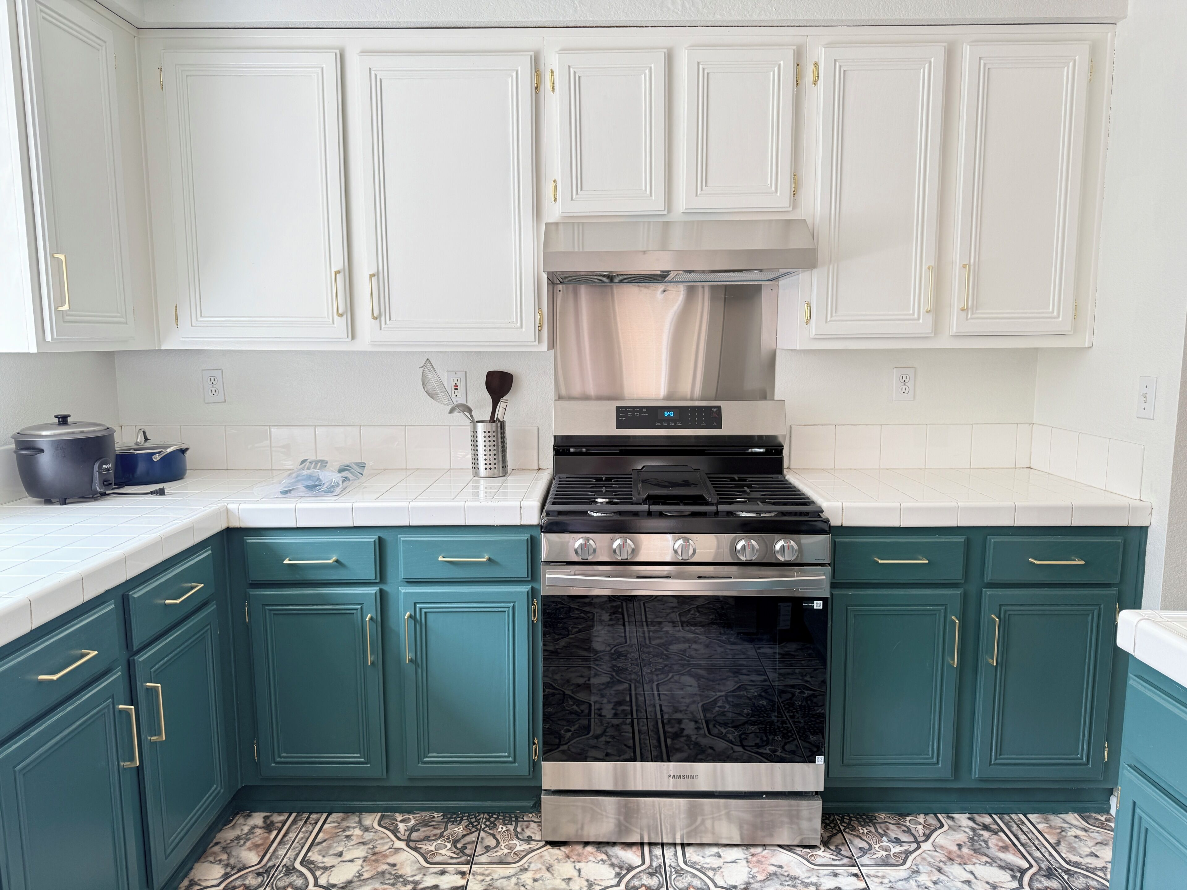 Une cuisine avec des meubles blancs, une cuisinière en acier inoxydable, des armoires de couleur turquoise et des carreaux de sol à motifs.