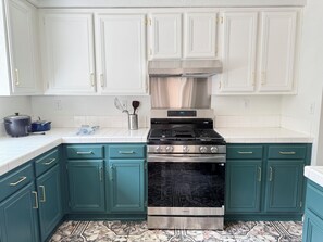 Una cocina con armarios blancos, estufa de acero inoxidable, muebles teal y baldosas de piso estampadas.