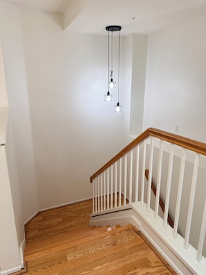 Una escalera con escalones de madera y barandillas blancas, que conduce a una plataforma con una pared blanca y una lámpara en el techo.
