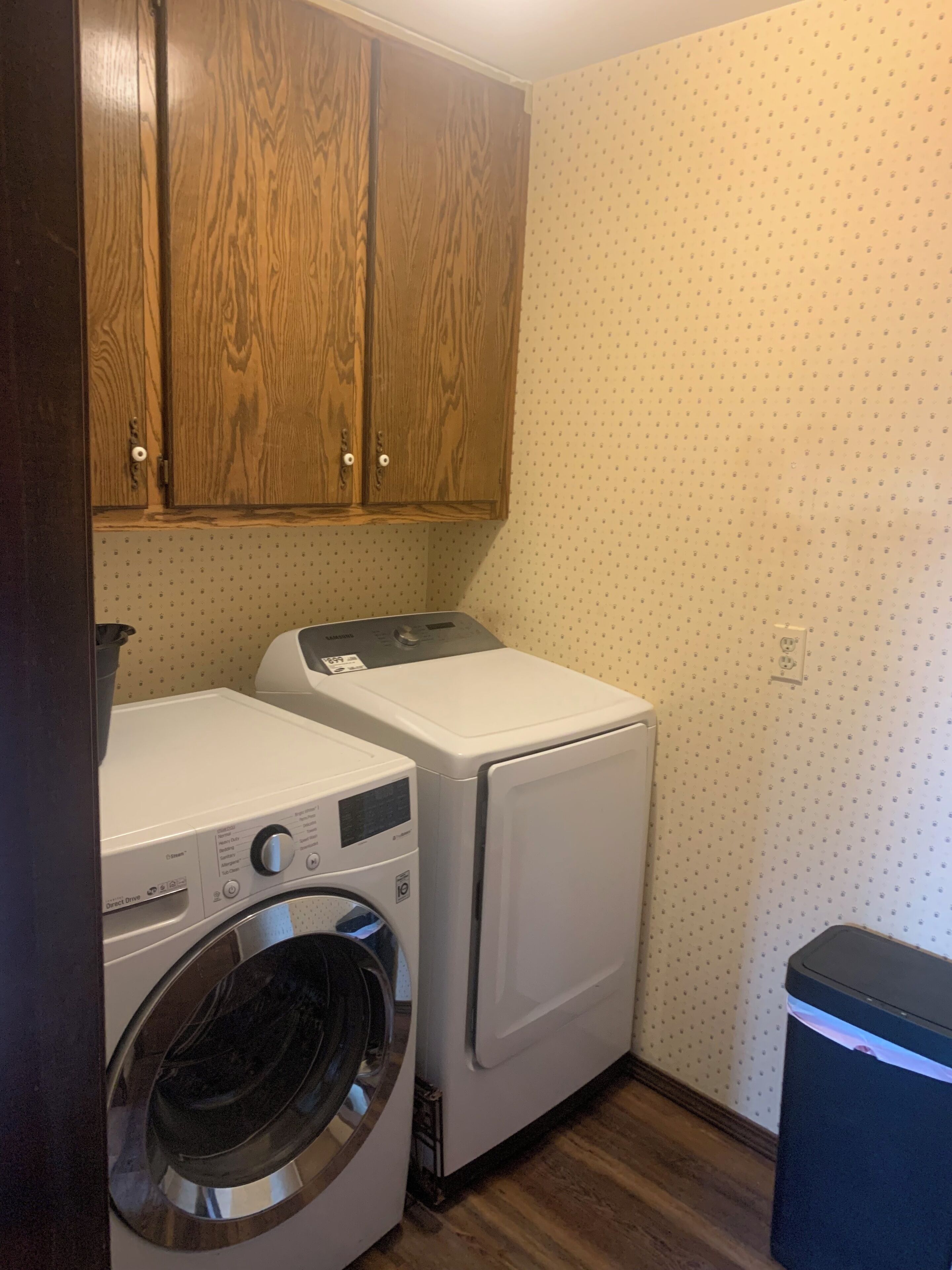 Un espace buanderie équipé d’un lave-linge et d’un sèche-linge à chargement frontal, de placards en bois au-dessus et d’un mur orné d’un motif.