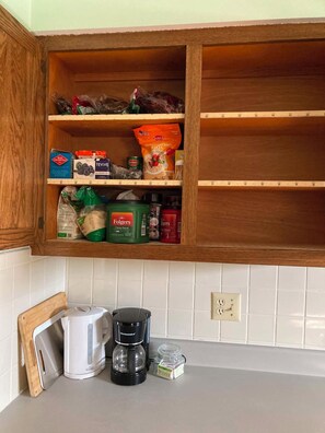 A kitchen with wooden cabinets, a white countertop, a coffee maker, and various food items. - 3-bedroom 2 bath -term rental 28+ days (Joplin)