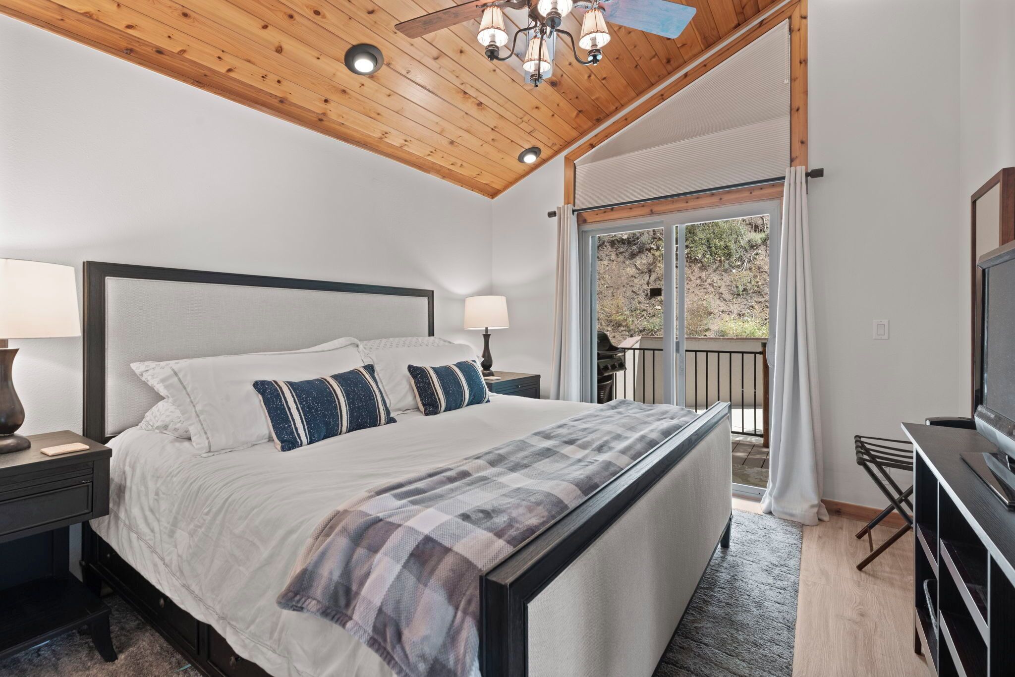 A bedroom with a large bed, a TV, and a balcony with curtains.