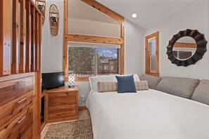 Ein Schlafzimmer mit einem Bett, einem Fernseher, Holzmöbeln, einem Fenster und einem Spiegel.